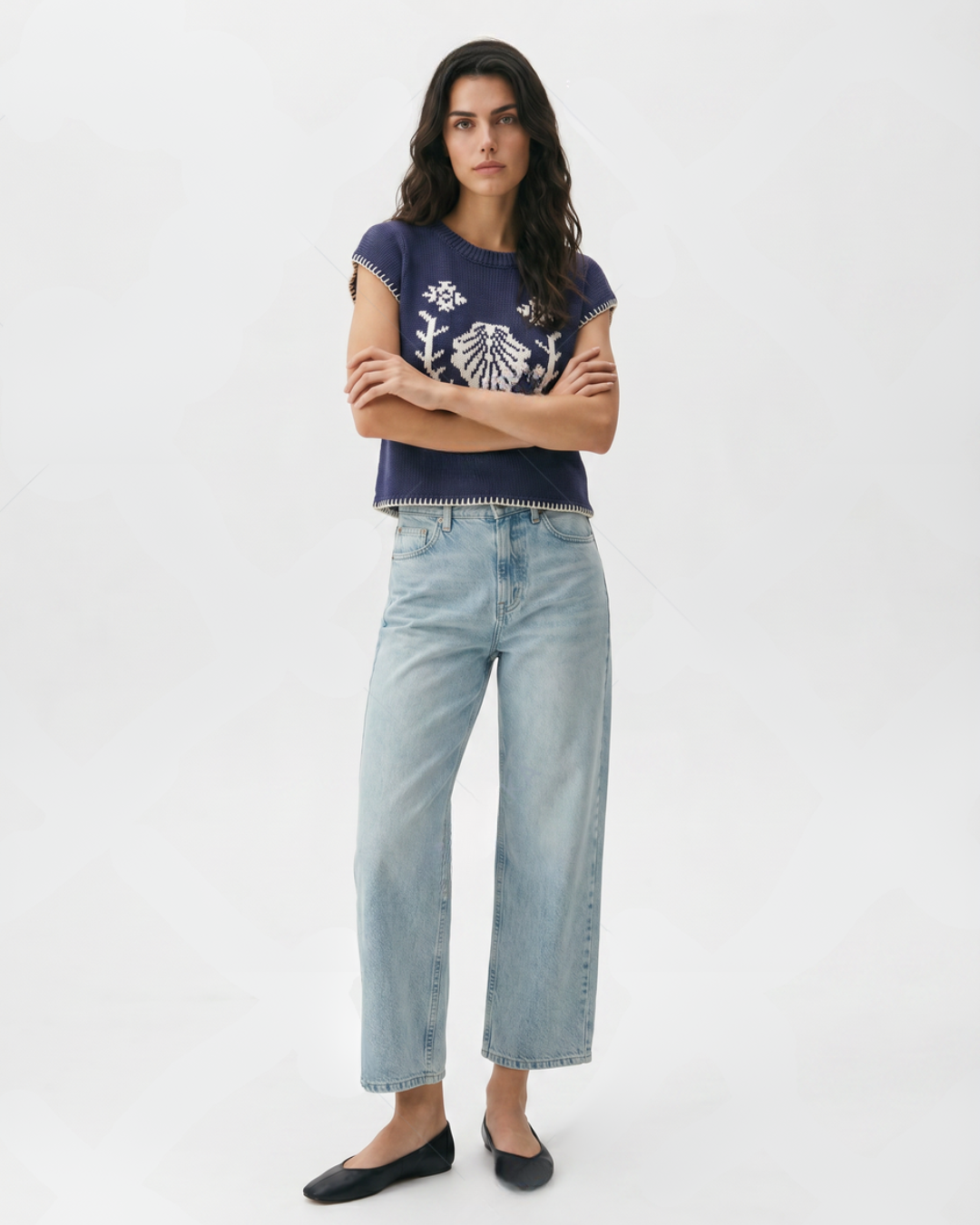 Woman wearing a navy blue top with white patterns and light blue jeans on a white background